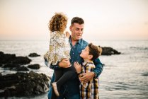 Uomo di mezza età con i suoi figli sulla riva del mare sorridendo e abbracciandosi — Foto stock
