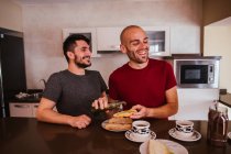 Cheerful gay couple having breakfast in kitchen at home — Stock Photo