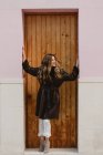 Smiling stylish woman in vintage leather coat standing near wooden door on street — Stock Photo