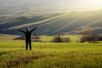 Back view of person in jacket with open arms in majestic green fields of Italy — Stock Photo