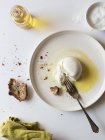 Piatto con deliziosa burrata fresca su tavolo bianco vicino a pezzo di pane e olio con sale — Foto stock