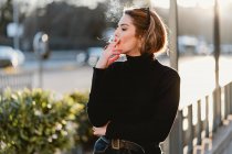 Pretty woman smoking cigarette on sunny street — Stock Photo