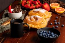 Fresh red apple and ripe blueberries placed on timber tabletop near mug of aromatic hot beverage and delicious bun for breakfast in morning — Stock Photo