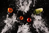 Левитация спелых овощей и салата в прозрачных брызгах воды на черном фоне — стоковое фото