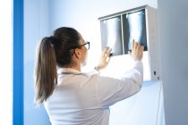 Молода жінка-лікар в уніформі дивиться на рентгенівське зображення на стіні в кімнаті — стокове фото