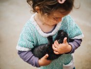 Tendre scène de mignonne petite fille tenant et berçant un petit chat noir — Photo de stock