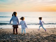 Kleine Mädchen Händchen haltend, während andere Schwester an einem Wintertag am Strand rennt — Stockfoto