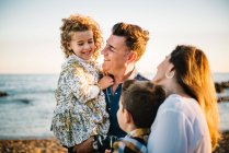Homem de meia idade uma mulher com filhos na costa do mar sorrindo e abraçando uns aos outros — Fotografia de Stock