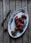 Plate of delicious ripe strawberries on wooden tabletop near metal knife — Stock Photo