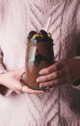 Femme sans visage en pull rose tenant un verre de smoothie au chocolat avec des noix et des bonbons — Photo de stock