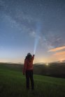 Vista posterior de la persona de pie en las verdes tierras altas y brillando con la antorcha en el cielo estrellado, Toscana, Italia - foto de stock