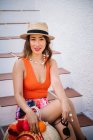 Молодая стильная китаянка в панамской шляпе и солнцезащитных очках сидит на лестнице и наслаждается ярким летним днем — стоковое фото