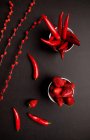 Червона тканина і гілки з яскравими бруньками розміщені на чорному тлі біля гострого перець чилі і солодкої стиглої полуниці — стокове фото