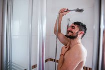 Hemdlos lächelnder Mann mit Dusche im Badezimmer — Stockfoto