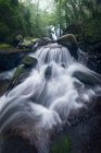 Пейзаж красивого водопада течет в условиях длительного воздействия на тяжелые валуны в диких лесах — стоковое фото