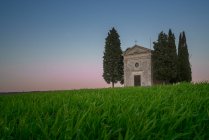 Paysage paisible de petite chapelle avec des cyprès dans un champ vert désert isolé au coucher du soleil en Toscane, Italie — Photo de stock