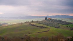Paysage majestueux de vallée verdoyante avec champs et chaîne de montagnes sous un ciel nuageux au coucher du soleil en Toscane, Italie — Photo de stock