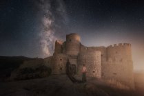 Silhouette einer Person, die in der Nähe geheimnisvoller Ruinen uralter Festung am nächtlichen Sternenhimmel steht — Stockfoto