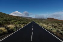 Asphalt countryside road through grassy terrain near snowy mountain peak on sunny day on Canary Islands, Spain — Stock Photo