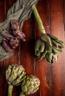 Alcachofas frescas maduras con servilleta sobre mesa de madera marrón - foto de stock