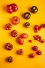 Различные спелые помидоры разбросаны на ярко-желтом фоне — стоковое фото
