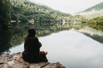 Жінка сидить з ковдрою біля озера і гір — стокове фото
