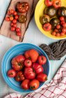 Holztisch mit Schalen mit verschiedenen frischen roten Tomaten — Stockfoto
