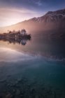 Paisagem de pacífico lago azul com casas em terra ao pôr-do-sol no fundo de montanhas ao sol, Suíça — Fotografia de Stock