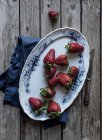 Teller mit leckeren reifen Erdbeeren auf hölzerner Tischplatte neben blauer Serviette und Metallmesser — Stockfoto