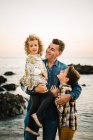 Чоловік середнього віку зі своїми дітьми на морському березі посміхається і обіймає один одного — стокове фото