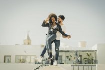 Multiracial hombre y mujer riendo y equilibrando en la pared mientras se divierten en la calle de la ciudad durante la fecha - foto de stock