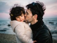 Cena fofa de pai segurando e beijando sua filhinha na praia no inverno — Fotografia de Stock
