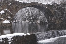 Fluss fließt im verschneiten Winterwald mit alter zerstörter Brücke — Stockfoto