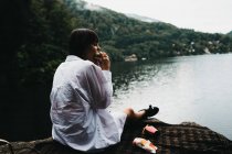 Femme manger hamburger près du lac et des montagnes — Photo de stock