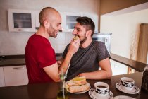 Feliz pareja gay desayunando en la cocina - foto de stock