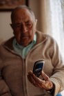Пожилой человек использует свой телефон в интерьере своего дома — стоковое фото