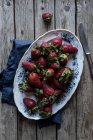 Plate of delicious ripe strawberries on wooden tabletop near blue napkin and metal knife — Stock Photo