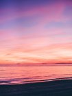 Vista desde la costa hasta la puesta de sol púrpura en el cielo nublado sobre el océano. - foto de stock