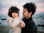 Linda escena de papá sosteniendo y abrazando a su hija pequeña en la playa en invierno - foto de stock