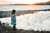 Unerkennbares Mädchen, das bei Sonnenuntergang am Strand steht — Stockfoto