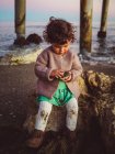 Cute kid playing with seashell by a pier at the beach — Stock Photo