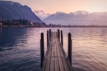 Molo di legno sopra il lago turchese in montagne innevate al tramonto della Svizzera — Foto stock