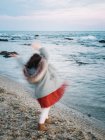 Anonymes kleines Mädchen, das sich am Strand bewegt und an einem Wintertag aufs Meer blickt — Stockfoto