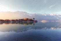 Landscape of peaceful blue lake with houses on shore at sunset on background of mountains in sunshine, Switzerland — Stock Photo