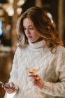 Стильная женщина пьет вино в баре и пользуется мобильным телефоном — стоковое фото