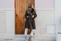 Femme élégante en cuir vintage manteau debout près de la porte en bois sur la rue — Photo de stock