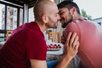 Лагідна гей пара цілується за столом з полуницею на кухні — стокове фото