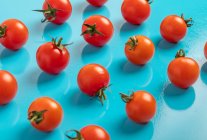 Frische reife Tomaten auf blauem Hintergrund verstreut — Stockfoto