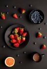 Различные свежие ягоды с грейпфрутом и кружка ароматного горячего напитка на завтрак на черном фоне — стоковое фото