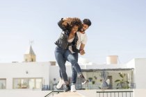 Мультирасовые мужчина и женщина смеются и балансируют на стене, веселясь на городской улице во время свидания — стоковое фото